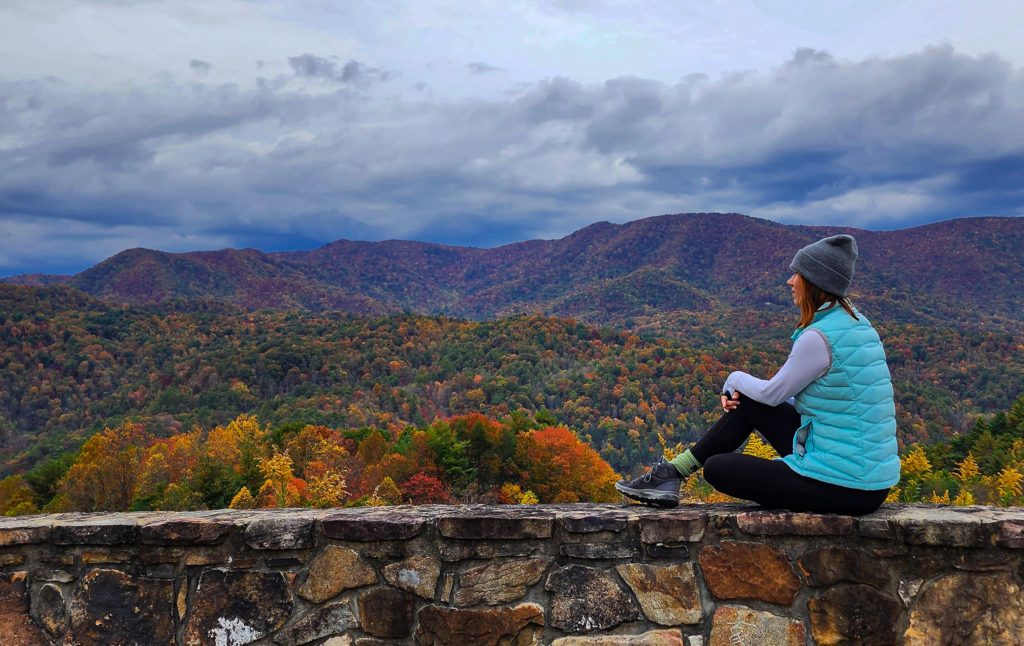 A woman in a vest sitting on the ledge of a scenic overlook in the Appalachia mountains in Tennessee.